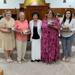 Women of the church standing together in the sanctuary, each holding a gift
